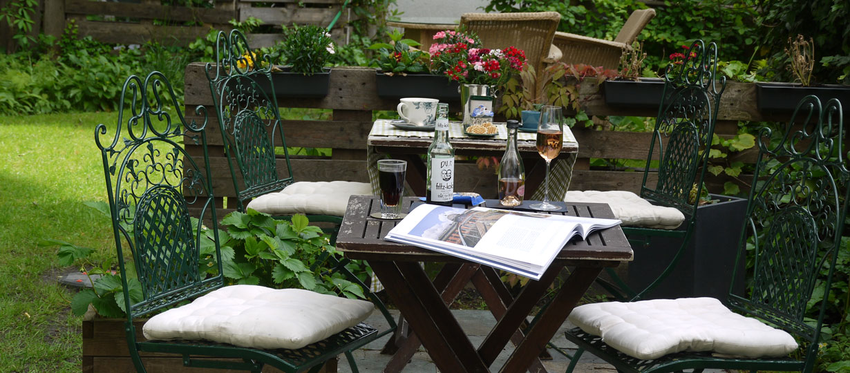 Hotelgarten mit Rosenbogen, Gartenmöbeln und altem Baumbestand